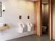 Moderne Wand mit zwei Urinalen in weiß, Holzregal mit Pflegeprodukten. Ideal Standard Betätigungsplatte in Chrom über den Urinalen montiert. Helle, strukturierte Wandgestaltung.